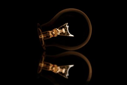 Image of lightbulb against a black background. Bulb is mirrored as it lies across the screen, fitting to the left, bulb and filament to the right